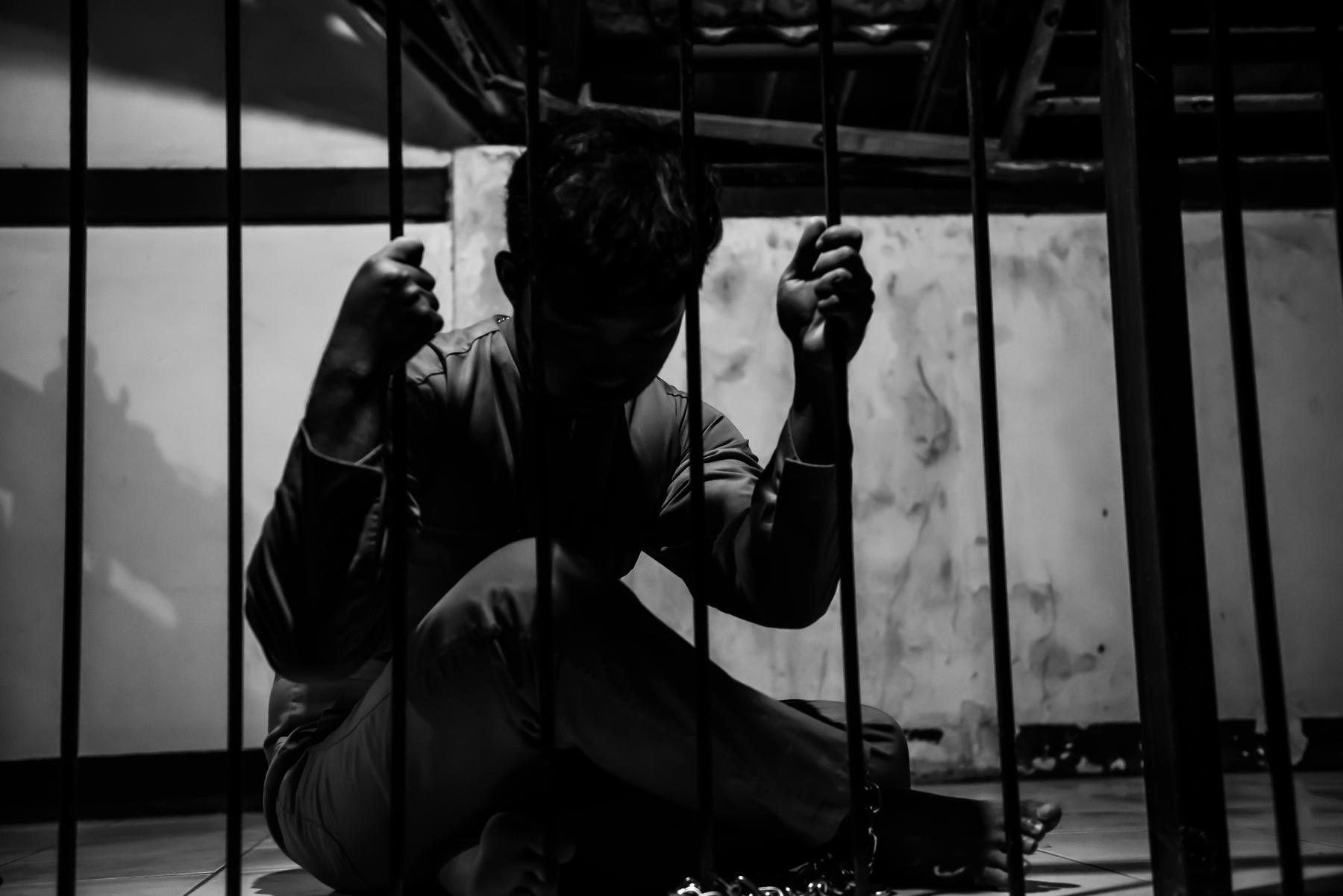 A young person sitting behind bars